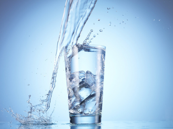 A stream of water pouring into and splashing around a tall glass with ice against blue background; concept is water and weight