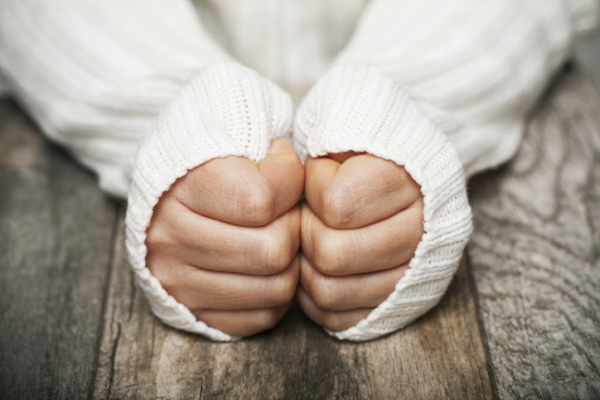 cropped photo of a person's hands clenched in fists, their sweater sleeves cover most of their hands, indicating that they are cold